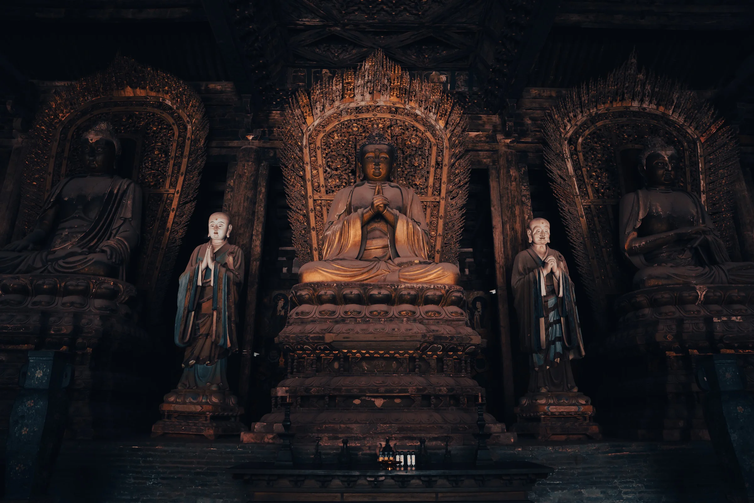 Three gilded Buddha statues in a darkened temple hall