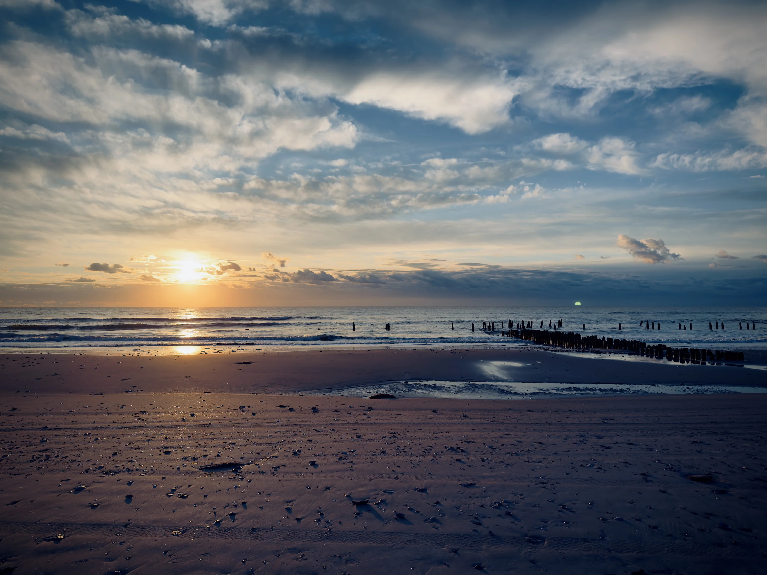 A pale sun setting over swimmers on the beach